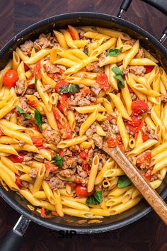 a skillet filled with pasta, meat and tomatoes on top of a wooden table