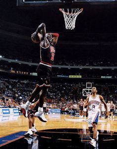 a basketball player jumping up to dunk the ball in front of another player who is going for it