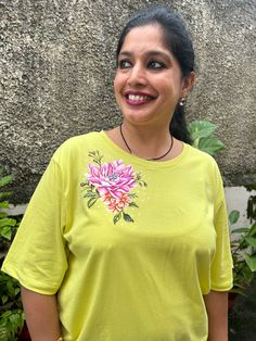 a woman standing in front of a stone wall with a flower on it's t - shirt