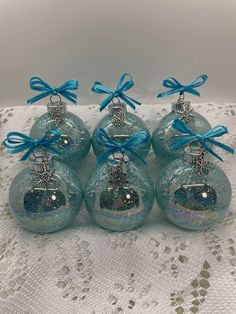 six glass christmas ornaments with blue bows and glittery decorations on white doily lace