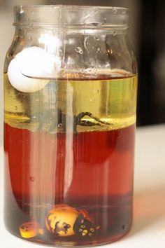 a jar filled with liquid sitting on top of a white table next to an orange and yellow object