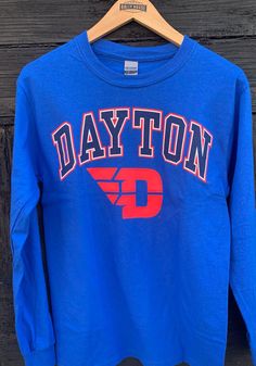 Show off your team pride in this Dayton Flyers Blue Arch Logo Long Sleeve T Shirt! This Dayton Long Sleeve Tee features a screen print of "Dayton" with Flyers logo across chest. Make sure everyone knows you root for the Flyers with this Blue Dayton T Shirt. Go Flyers!! Classic fit, Seamless double needle 7/8" collar, Taped neck & shoulders, Ribbed cuffs, Unisex, Fit: True to Size, 100% Cotton Long Sleeve Cotton T-shirt With University Logo, University Logo Long Sleeve Cotton T-shirt, Blue Long Sleeve T-shirt For School Spirit, Blue Long Sleeve T-shirt For College, Blue Long Sleeve Fan Merchandise T-shirt, Blue Long Sleeve T-shirt With Team Spirit, Blue Long Sleeve T-shirt For Sports Events, Dayton Flyers, Arch Logo