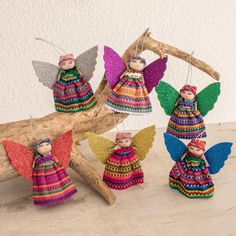 four colorful angel ornaments hanging from a tree branch on top of a wooden table next to a white wall