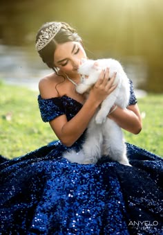 a woman in a blue dress holding a white cat while wearing a tiara on her head