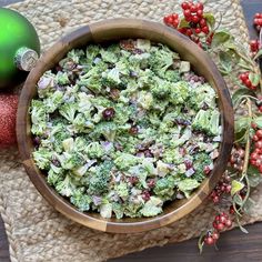 a wooden bowl filled with broccoli and cranberries next to a christmas ornament