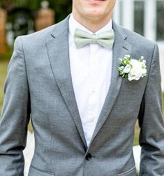 a man in a gray suit and bow tie is standing outside with his hands in his pockets