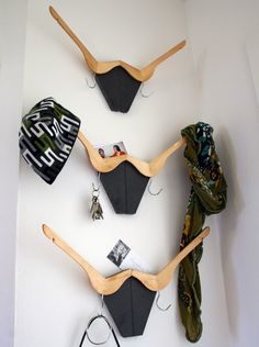 three wooden bras hang on the wall with scarves and hats hanging from them