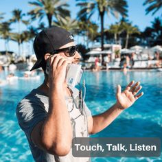 a man talking on a cell phone next to a swimming pool with palm trees in the background