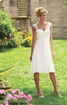 a woman standing in the grass wearing a white dress