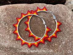 two hoop earrings with red and yellow designs on them sitting on a rock in the grass