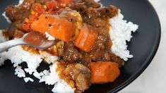 a black plate topped with rice and meat covered in gravy on top of it