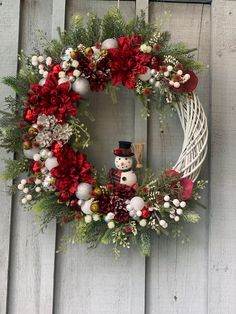 a christmas wreath hanging on the side of a wooden door with snowman and red flowers