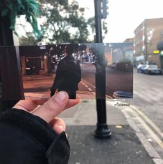 a person holding up a polaroid with a street scene in the background