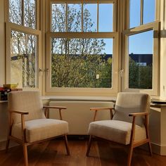 two chairs sitting next to each other in front of a window with the view of trees outside