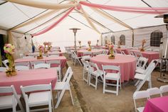 tables and chairs are set up under a tent for an outdoor wedding reception with pink tablecloths