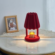 a red lamp sitting on top of a white table next to a framed photo and a candle holder