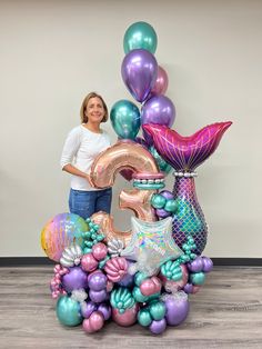 a woman standing next to a large number balloon sculpture in the shape of a mermaid