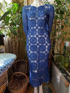 a mannequin wearing a blue crochet dress in front of a potted plant