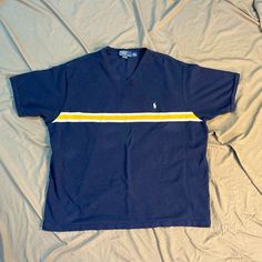 Vintage 90's Polo By Ralph Lauren Collarless Polo V-Neck XXL  Navy shirt with yellow and white stripe on front and back White pony on left breast Excellent Condition  100% Cotton Flat Lay Measurements: Chest 25" Length 26" Cotton V-neck Tops With Contrast Stripes, Cotton V-neck Top With Contrast Stripes, Sporty Striped V-neck Top, Summer V-neck Top With Contrast Stripes, Retro Striped V-neck Top, Striped Cotton V-neck T-shirt, 90s Striped Short Sleeve Tops, Navy Shirt, Ralph Lauren Polo