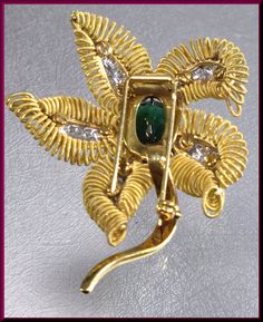 "The captivating flower brooch has a center oval shaped 10.00 ct deep forest green tourmaline. It dates from the 1960's. It is surrounded by 4 gold coiled leaves encrusted with 1.75 ct of round diamonds in the center of each leaf. It all gracefully blooms out of the golden stem. This is enticing appeal all swathed up into a pin. The pin weighs 45 grams. It measures 2 ½ \" long and 2\" wide at its widest point. P 518S SIX MONTH LAY-AWAY AVAILABLE - PLEASE CONTACT ME TO SET UP A PLAN" Elegant Green Gemstone Brooch, Elegant Green Gemstone Brooches, Elegant Green Flower Brooches, Elegant Green Oval Brooches, Green Oval Brooches For Formal Occasions, Brooch Diamond, Brooch Flower, Bouquet Gift, Bouquet Bridal