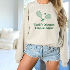 Elevate your tennis game with our 'World's Okayest Tennis Player' crewneck sweatshirt.  The graphic design features a humorous twist on the classic tennis motif. Instead of the usual perfectly aligned tennis rackets and centered ball, our design features two tennis rackets and a tennis ball that are slightly off-centered. It's a fun and lighthearted take on the game, perfect for the "okayest" tennis players who embrace their average skills, unique style and sense of humor. This cozy, heavy blend Tennis Crew Neck Top With Logo Print, Logo Print Crew Neck Tennis Tops, Sporty Tennis Sweatshirt With Graphic Print, Crew Neck Tennis Top With Logo Print, Cotton Tennis Sweatshirt With Relaxed Fit, Cotton Tennis Sweatshirt In Relaxed Fit, Tennis Graphic Print Sweatshirt For Sports Season, Tennis Graphic Print Sweatshirt, Sporty Long Sleeve Sweatshirt For Tennis