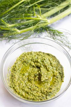 a glass bowl filled with pesto next to green onions and celery stalks