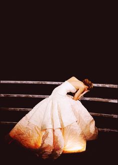 a woman in a white dress leaning on a fence