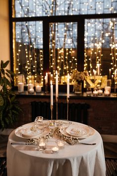 the table is set with white plates and silverware, lit by candles in front of a window