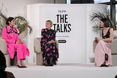 two women sitting on chairs talking to each other in front of a white wall with plants