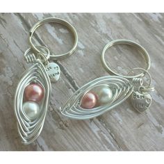 two silver and pink pearls are hanging from the ends of keychains on a wooden surface