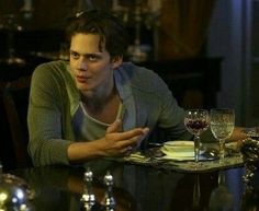 a young man sitting at a table with wine glasses on it and looking to his left