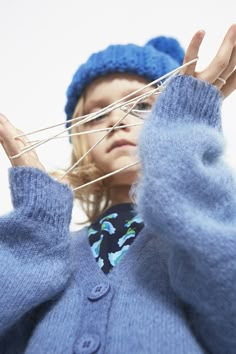 a woman wearing a blue hat and sweater holding up clothes pins