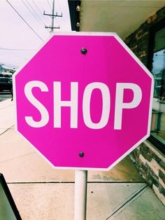 a pink stop sign sitting on the side of a road next to a store front