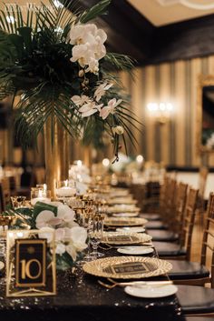 a long table set with black and gold plates, place settings and centerpieces