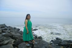 a woman in a green dress standing on rocks near the ocean