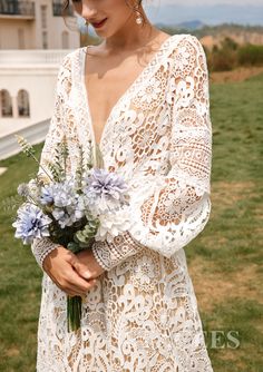 a woman wearing a white lace dress holding a bouquet of flowers in front of a house