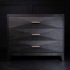 a black and gold chest of drawers with two handles on each drawer, in front of a dark background