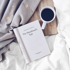 there is a book on the bed next to a cup of coffee and a blanket