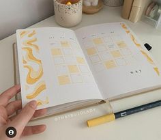 a hand holding an open book on top of a desk next to a pen and candle