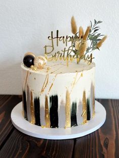 a white and black cake with gold lettering on it sitting on a wooden table next to a wall