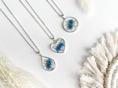 Our Forget-Me-Not Flower Pendant Necklace is made with 18k gold plating.  The silver pendant is 925 silver plated.   Each pendant holds delicate dried pressed Forget-Me-Not flowers, safely encased in clear resin and adorned with beautiful Queen Anne's lace and glittering gold flakes. 🌸 This necklace is perfect for any occasion, whether you're attending a fancy event like a wedding or simply hanging out with friends; it's the perfect accessory. Its simple, elegant style pairs well with everythin Blue Flower Charm Jewelry As Gift For Her, Blue Flower Pendant Necklace Gift For Her, Blue Flower Pendant Necklace For Her, Blue Flower Pendant Necklace As A Gift For Her, Silver Flower-shaped Jewelry With Pressed Flowers, Blue Flower-shaped Jewelry For Mother's Day, Silver Jewelry With Pressed Flowers In Flower Shape, Silver Jewelry With Pressed Flowers, Blue Flower Shaped Jewelry For Mother's Day