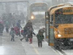 people walking in the snow next to two school buses and one bus is on the street