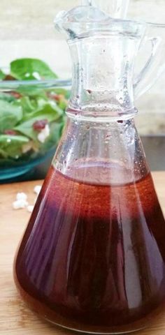 a glass pitcher filled with liquid sitting on top of a wooden table next to a salad