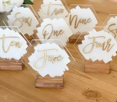 place card holders with gold foil lettering on them sitting on a wooden table next to flowers