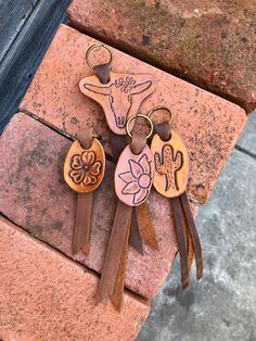 two cow key chains are sitting on top of a brick wall, one has a flower and the other has a leather tassel