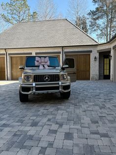 a mercedes benz is parked in front of a house with a pink bow on the hood