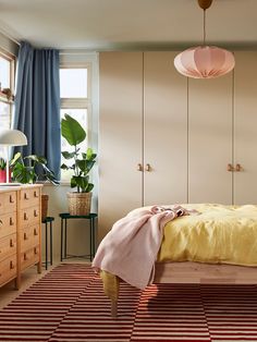 a bed room with a neatly made bed next to a dresser and a lamp hanging from the ceiling