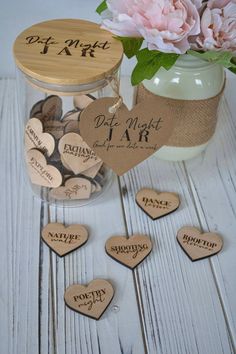 a jar filled with lots of wooden hearts next to pink flowers on top of a white table