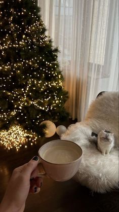 a person is holding a coffee cup in front of a christmas tree