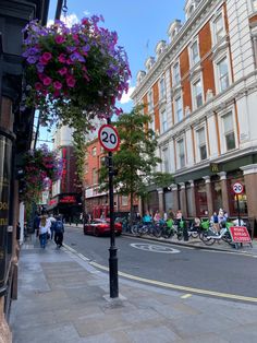 people are walking down the street in front of tall buildings and flowers hanging over the sidewalk